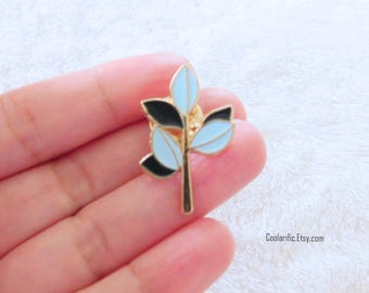 Puede incluir: Un pin de tono dorado con un diseño de hoja estilizado en azul y negro.