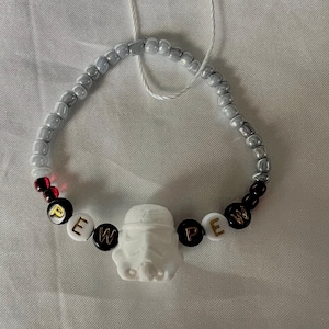 May include: A white beaded bracelet with black and white letter beads spelling "PEW PEW" and a white plastic Stormtrooper head charm.