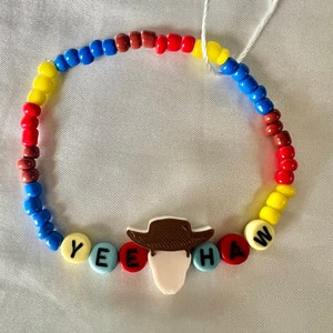 May include: A colourful beaded bracelet with the word "YEEHAW" spelled out in letter beads and a cartoon image of Woody from Toy Story in the centre.