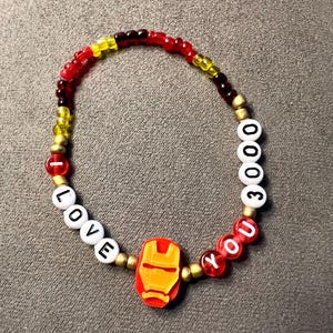 Puede incluir: Una pulsera de cuentas rojas, amarillas y negras con cuentas de letras blancas que deletrean "I LOVE YOU 3000" y un dije de personaje de Iron Man rojo y amarillo.