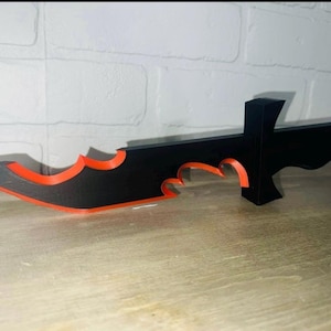 May include: A black and red plastic knife with a serrated blade and a handle. The knife has a sharp point and a curved blade.