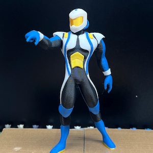 Op de afbeelding: Een 3D-geprint actiefiguur van een futuristisch personage. Het figuur is voornamelijk zwart met witte, blauwe en gele accenten. Het heeft een helm, een nauwsluitend pak en blauwe handschoenen en laarzen. Het figuur poseert met één arm uitgestrekt.