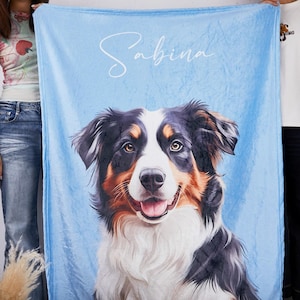 Puede incluir: Una manta azul claro con un retrato de perro. El perro tiene pelo negro, marrón y blanco. El nombre "Sabina" está escrito en cursiva en la parte superior de la manta.