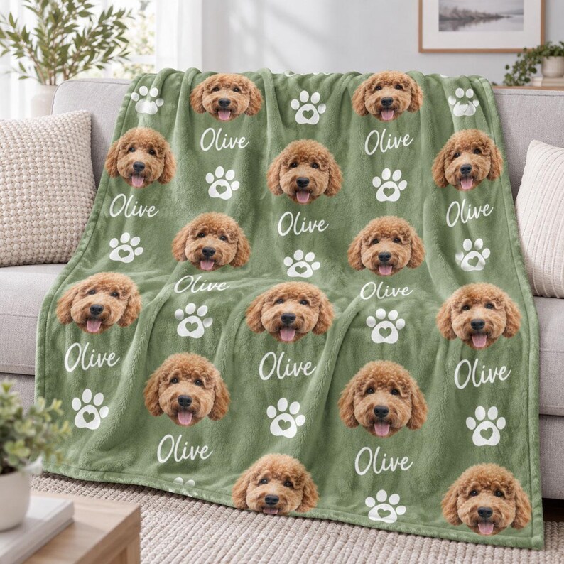 May include: A sage green fleece blanket featuring a repeating pattern of a golden doodle dog's face, white paw prints, and the name Olive written in a white script font. The soft fabric displays multiple portraits of the same dog.