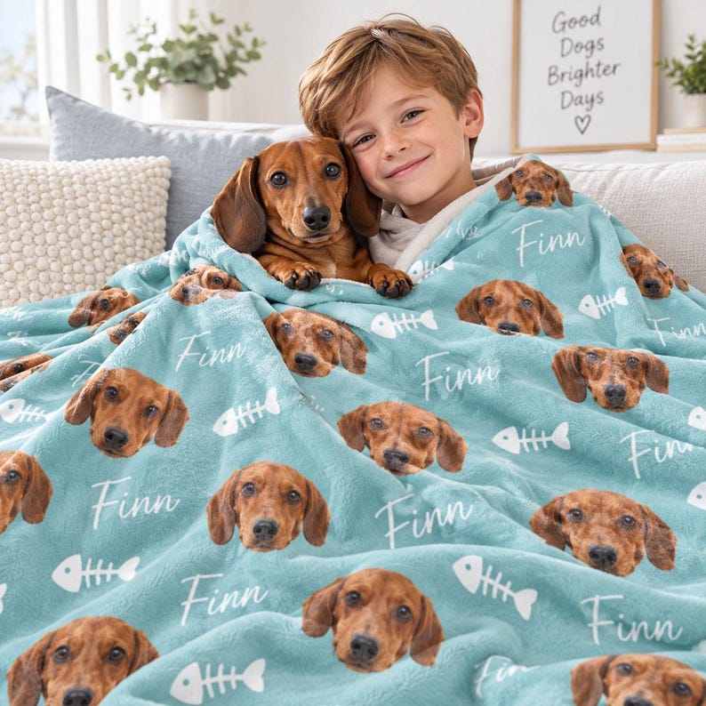 May include: A light blue fleece blanket featuring a repeating pattern of a brown dachshund dog face, the name Finn in white script, and white fish bone icons. The soft fabric displays multiple instances of the dog's portrait and the name.