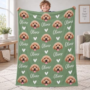 May include: A sage green fleece blanket featuring a repeating pattern of a golden doodle dog's face, white hearts, and the name Oliver written in a white cursive script. The design is printed across the entire surface of the soft fabric.
