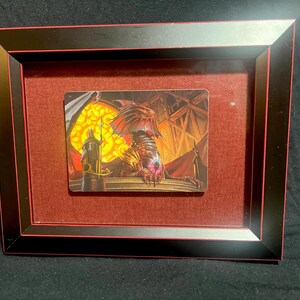 May include: A framed fantasy art print featuring a red dragon with a glowing eye, perched on a stone ledge. A human figure with a spear stands in the background.