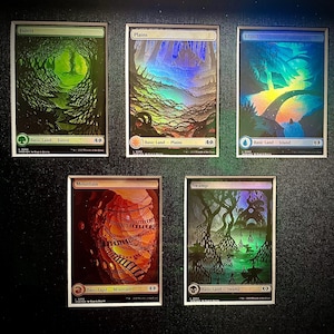 May include: Five Magic: The Gathering cards, each featuring a different basic land type: Forest, Plains, Island, Mountain, and Swamp. The cards are foil and have a holographic effect.