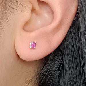 Op de afbeelding: Een close-up van een oor met een kleine roze edelsteen oorbel.