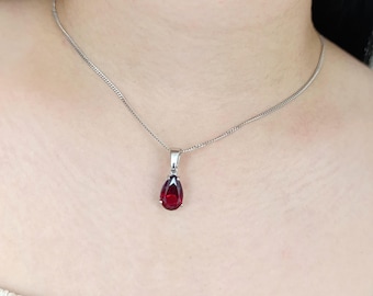 Può includere: Una collana d'argento con un pendente a forma di goccia, rosso intenso. Il pendente è incastonato in una lunetta d'argento e pende da una delicata catena d'argento. La collana è mostrata su uno sfondo neutro.