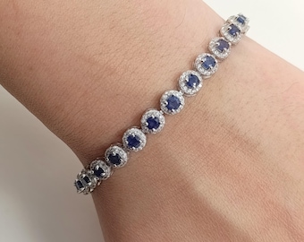 May include: A silver bracelet with a row of oval-shaped blue gemstones surrounded by smaller clear gemstones.