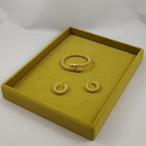 May include: A gold-toned jewelry set consisting of a flexible coil bracelet and a pair of matching hoop earrings. The bracelet features two smooth spherical end caps, while both the bracelet and the hoop earrings have a textured, beaded surface.