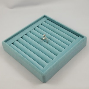 Peut inclure: Une bague ouverte argentée dotée de deux petites extrémités sphériques et d'un anneau torsadé texturé. La bague est placée au centre d'un plateau de présentation à bijoux carré en velours bleu clair avec plusieurs fentes rembourrées.
