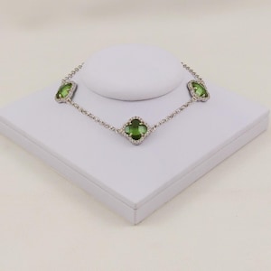 以下が含まれることがあります： 銀色のチェーンブレスレットで、3つのクローバー型のチャームが付いています。各チャームには半透明の緑色の石がはめ込まれており、その周りを小さく透明な輝く石が縁取っています。ブレスレットは繊細なリンクチェーンのデザインで作られています。