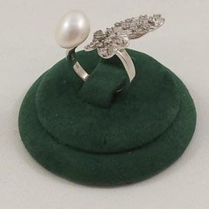 May include: A silver-toned open ring featuring a single white oval pearl on one end and a textured, leaf-shaped element encrusted with small clear stones on the other. The band is polished silver-toned metal, creating a bypass style design.
