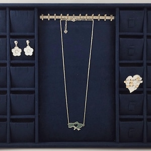 May include: A navy blue jewellery display case with various items of jewellery. Includes a silver necklace with a heart pendant, flower earrings, and a heart-shaped brooch. The case has multiple compartments for storage.