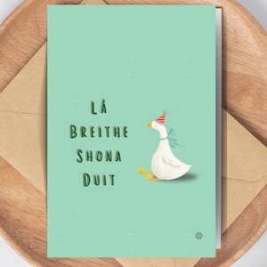 May include: A greeting card with a light green background, featuring text and a cartoon goose wearing a party hat. The card is on a wooden tray with a brown envelope.