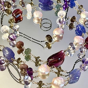 Puede incluir: Un collar de múltiples hilos con una variedad de piedras preciosas, incluyendo amatista, topacio azul y perlas. El collar está hecho con cadenas de oro y plata.