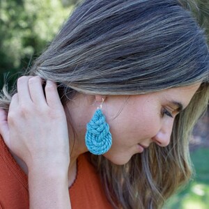 May include: Teal blue knotted teardrop earrings. The earrings are made of a woven material and hang from silver hooks.