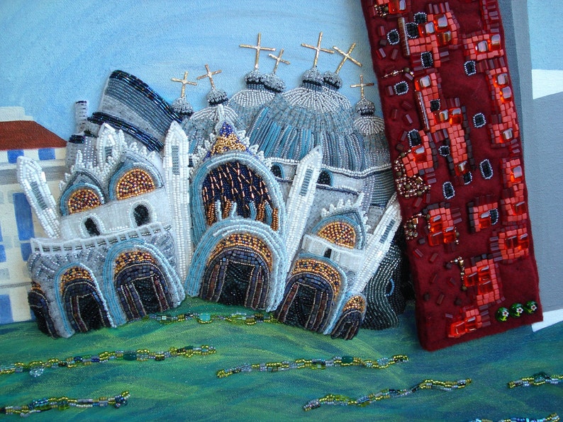 May include: A beaded artwork depicting a cityscape with multiple white buildings with blue and gold accents. The buildings have domes and crosses on top. The background is a light blue sky. A red beaded panel is on the right side of the image.
