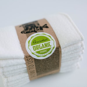May include: A stack of white organic cotton cloths with a brown paper label that says "Guaranteed Organic Fabric" and "How to Use".