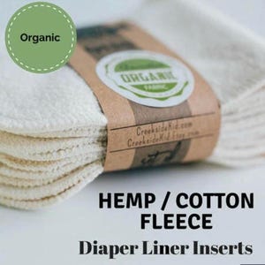 May include: A stack of organic hemp and cotton fleece diaper liner inserts. The inserts are white and have a soft, textured surface. The packaging is brown with the words "Organic" and "CreeksideKid.com" printed on it.