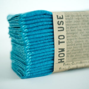 May include: A stack of teal blue reusable cloths with a brown paper label that reads "HOW TO USE" and includes instructions for using the cloths. The label also includes the text "FAMILY CLOTA WIPES."
