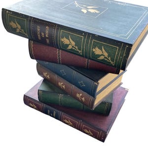 May include: A stack of five hardcover books with decorative spines. The top book is dark green with gold floral accents and the text HISTORY OF THE WORLD. Other books in the stack feature deep red, blue, and green covers with gold embossed details.