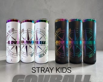 Puede incluir: Varios vasos aislados, algunos blancos y otros negros, con un diseño de rosa de los vientos y el texto "STRAY KIDS GOURBALL LIMITED EDITION". Los vasos tienen detalles iridiscentes y bordes de arcoíris.