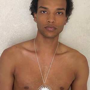 Puede incluir: Un collar de cadena de plata con un gran colgante redondo blanco en forma de sol.