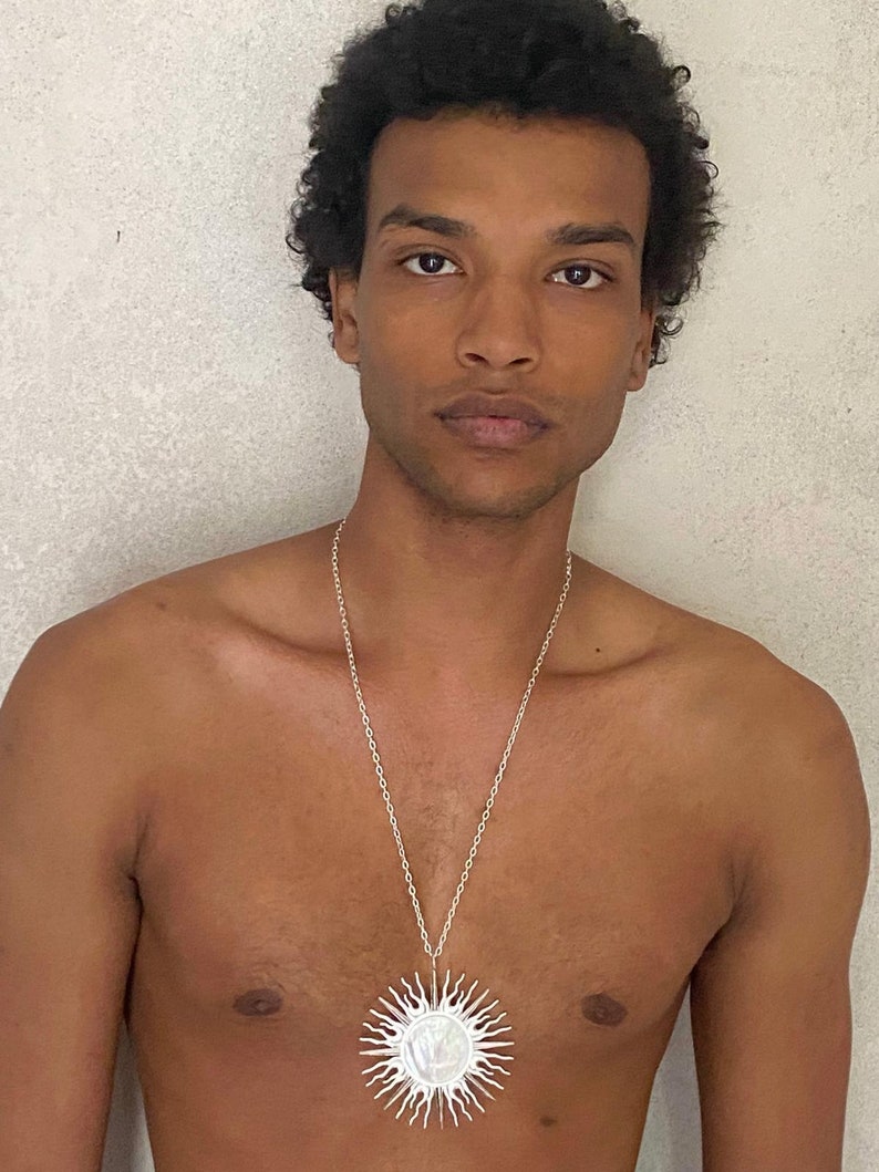 Puede incluir: Un collar de cadena de plata con un gran colgante redondo blanco en forma de sol.