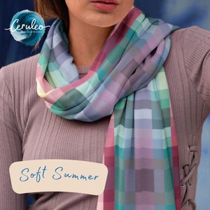 Może przedstawiać: Kobieta w długim, malinowym swetrze z szalem w kratę w odcieniach różowego, niebieskiego, zielonego i szarego. Szal jest zawiązany wokół szyi i opada na klatkę piersiową. Tekst "Soft Summer" jest napisany na białym tle na beżowym tle.