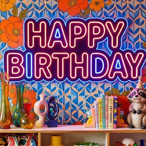 May include: A neon sign displaying the text HAPPY BIRTHDAY in bright pink and blue light. The sign is mounted on a wall with a vibrant orange and blue floral wallpaper pattern, positioned above a shelf containing various decorative glass vases.