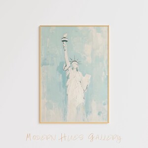 May include: A painting of the Statue of Liberty in a light blue and white color scheme. The painting is framed in a gold frame. The text "MODERN HUES GALLERY" is written in cursive at the bottom of the image.