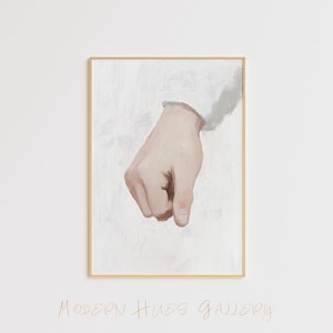 May include: A framed art print featuring a hand in a downward gesture. The hand is painted in realistic tones against a textured white background. The frame is a thin, gold color. The text "MODERN HUES GALLERY" is written in a cursive font.
