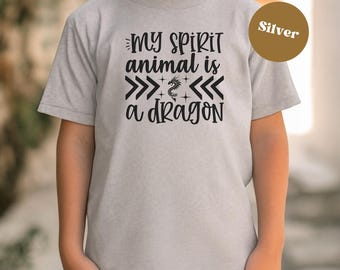May include: A light gray t-shirt with the text "MY SPIRIT animal is a DRAGON" in black. The design includes arrows and a dragon graphic. A silver-colored circle is in the upper right corner.