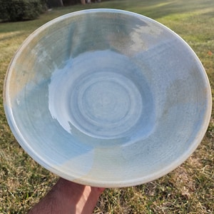 May include: A large, light blue ceramic bowl with a white glaze. The bowl has a subtle swirl pattern and a slightly uneven rim.