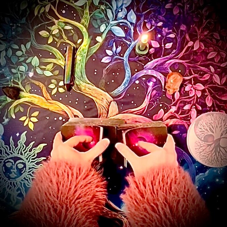 Pode incluir: Uma tape&ccedil;aria colorida com uma &aacute;rvore com galhos e folhas de arco-&iacute;ris. O fundo &eacute; escuro, com motivos celestiais. As m&atilde;os de uma pessoa seguram uma caixa escura com luzes rosas.