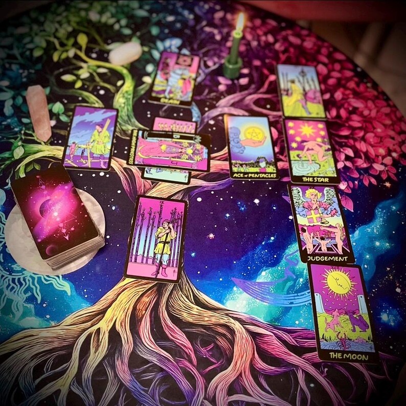 Pode incluir: Uma configura&ccedil;&atilde;o de leitura de cartas de tar&ocirc; em uma mesa redonda. A mesa &eacute; coberta com um pano colorido com um design de &aacute;rvore da vida e um c&eacute;u estrelado. As cartas de tar&ocirc; est&atilde;o dispostas, com um baralho vis&iacute;vel. Uma vela verde acesa e cristais tamb&eacute;m est&atilde;o presentes.