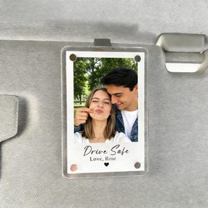 Peut inclure: Un cadre photo en acrylique transparent avec une photo d'un couple. La photo porte les mots "Drive Safe" et "Love, Rose". Le cadre est maintenu en place par un clip métallique.