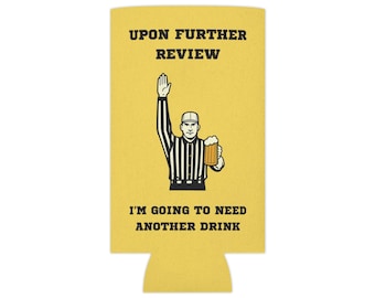 May include: Yellow beer can cooler with a referee illustration. The referee is holding up their hand and a beer mug. Text on the cooler reads "UPON FURTHER REVIEW" and "I'M GOING TO NEED ANOTHER DRINK."