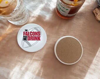 Puede incluir: Posavasos de cerámica blanco con una pelota de fútbol gris y el texto "The Falcons Make Me Drink".
