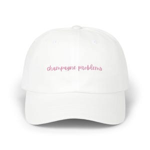 Può includere: Cappellino da baseball bianco con il testo "champagne problems" ricamato in rosa.
