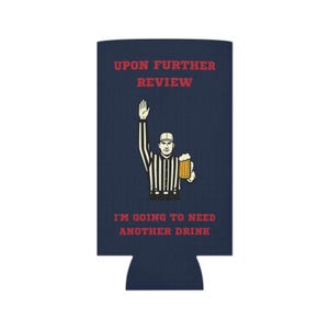 May include: Navy blue can cooler with the text "UPON FURTHER REVIEW" and "I'M GOING TO NEED ANOTHER DRINK" in red. The design features a referee holding a beer. A fun accessory for sports fans.