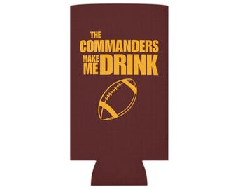 May include: A brown can cooler with the text "The Commanders Make Me Drink" in gold lettering and a gold football graphic.