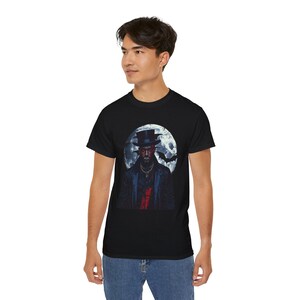 May include: A black t-shirt with a graphic print of a man in a top hat and coat standing in front of a full moon. Bats fly around the moon.