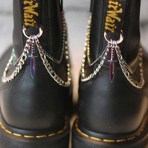 May include: Black leather boots with silver chains and rainbow-colored dagger charms attached to the back of the boots. The boots have a yellow tag that says "Air Mail" on the back.