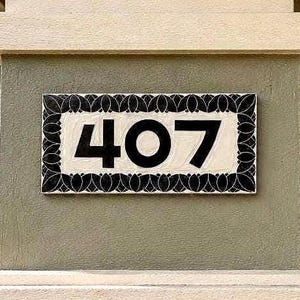 May include: A rectangular house number plaque displaying the digits 407 in bold black font against a cream-colored background. The plaque features a decorative black border with a repeating leaf-like pattern surrounding the central numbers.