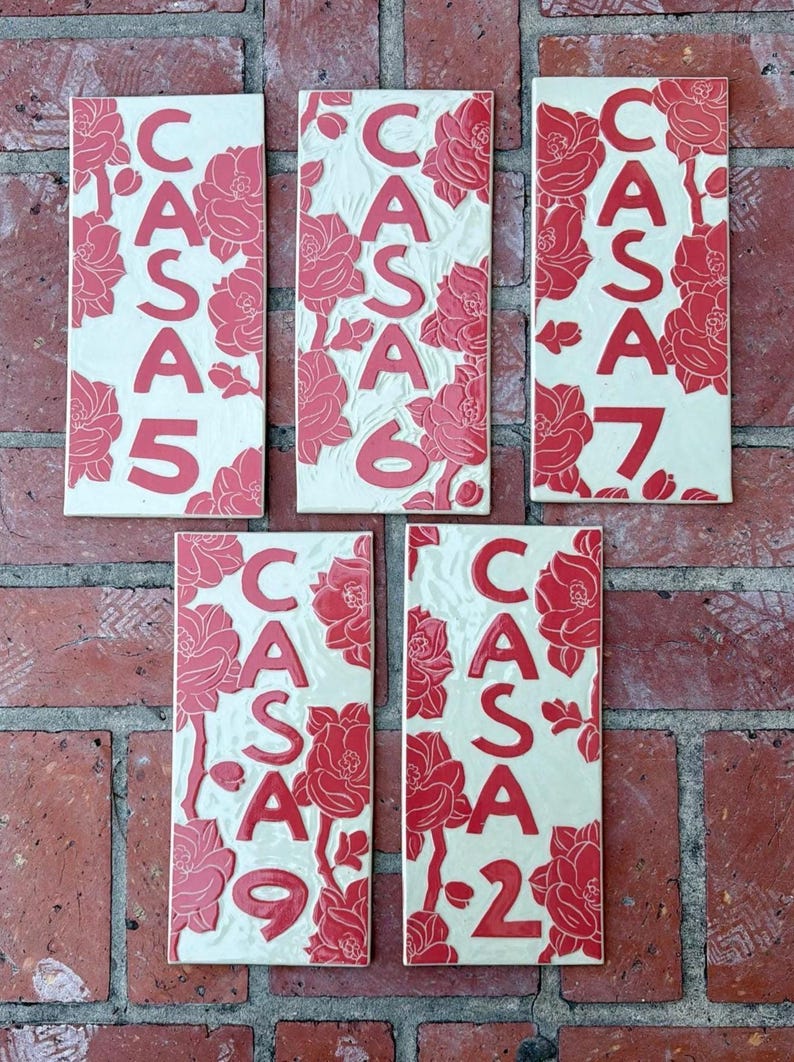 May include: Five rectangular ceramic tiles featuring a cream-colored background with embossed red floral patterns and the text CASA 5, CASA 6, CASA 7, CASA 9, and CASA 2. Each tile displays a unique arrangement of red flowers and bold red lettering.