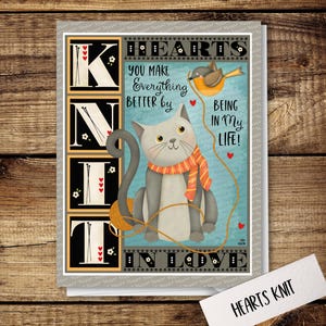 May include: A gray cat with orange and white stripes around its neck sits on a blue background with a ball of yarn. The cat is holding a string in its paw. The background has the words "Hearts Knit" and "You make everything better by being in my life!" in black text.